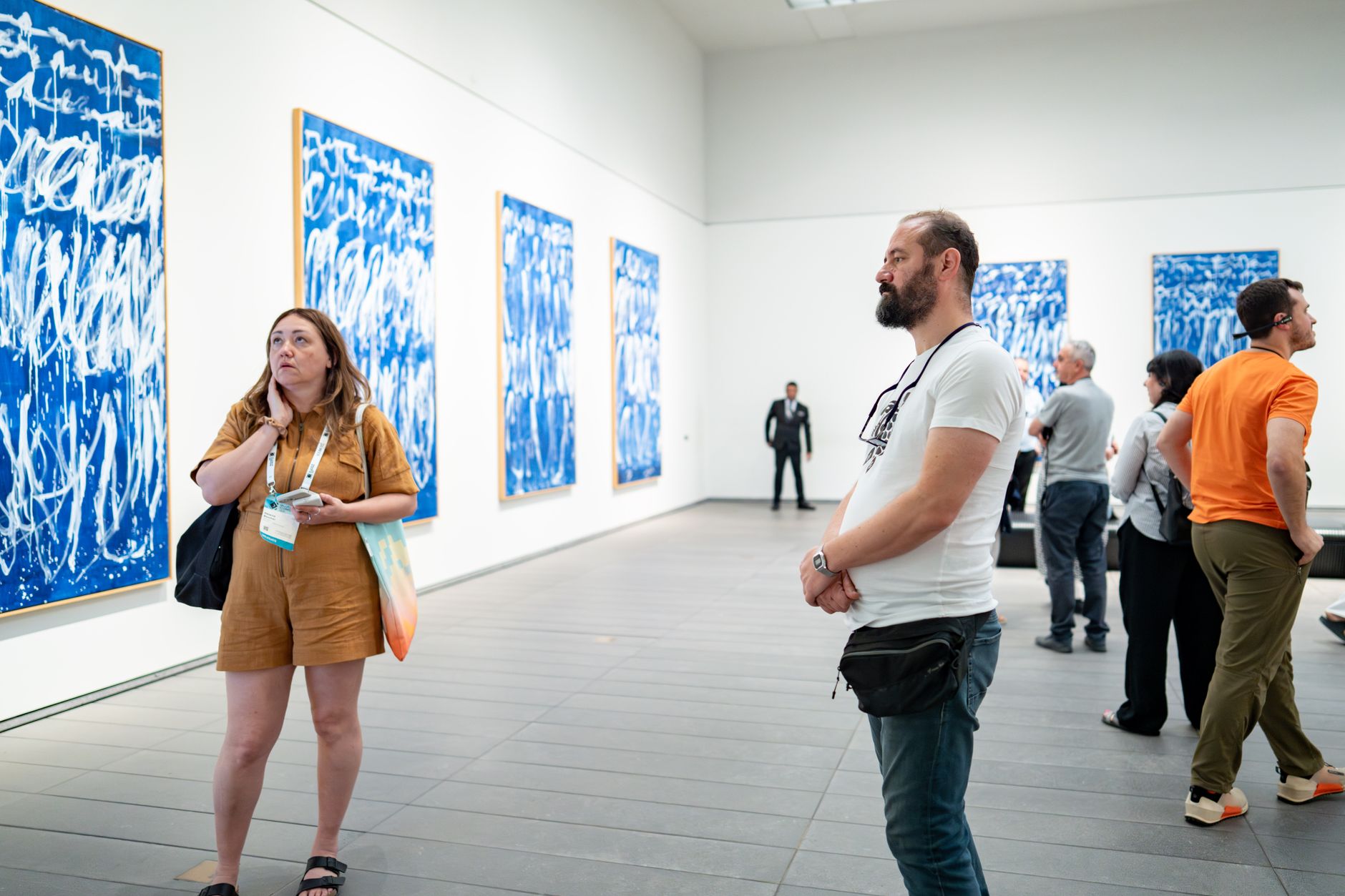 Des visiteurs contemplent des œuvres abstraites bleues dans une galerie d'art.
