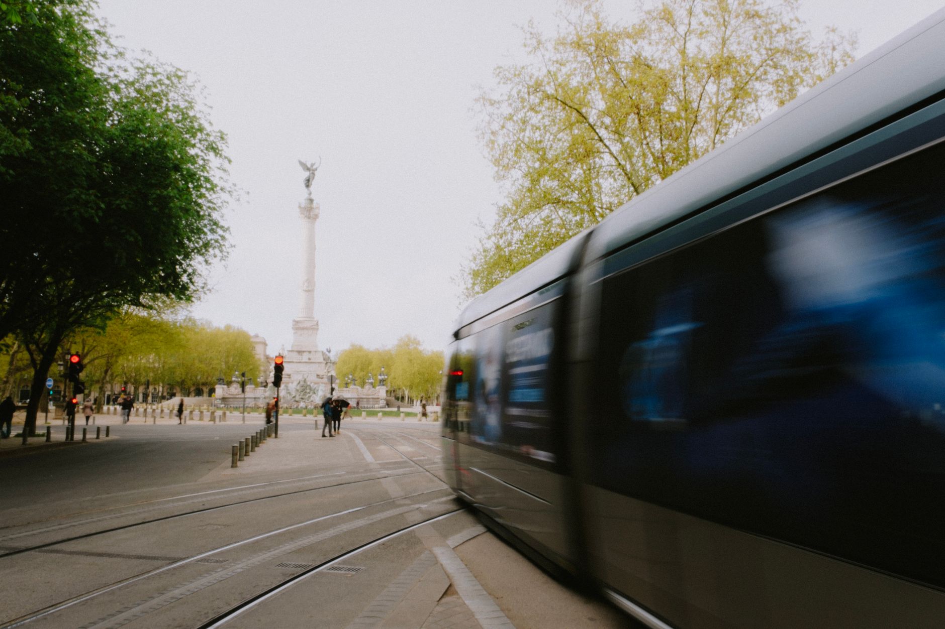 Blurred tram passes the Girondins Monument in a vibrant city street of Bordeaux, France.