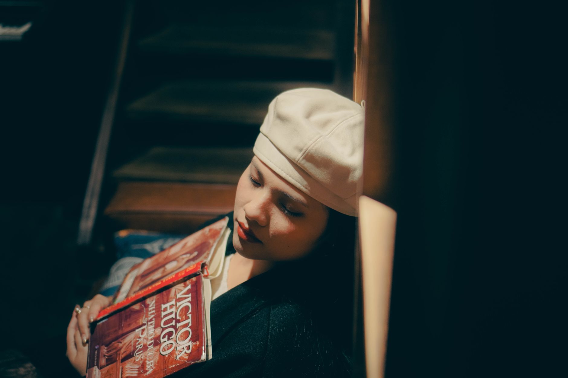 Woman with a beret holding Victor Hugo books, sitting on stairs.