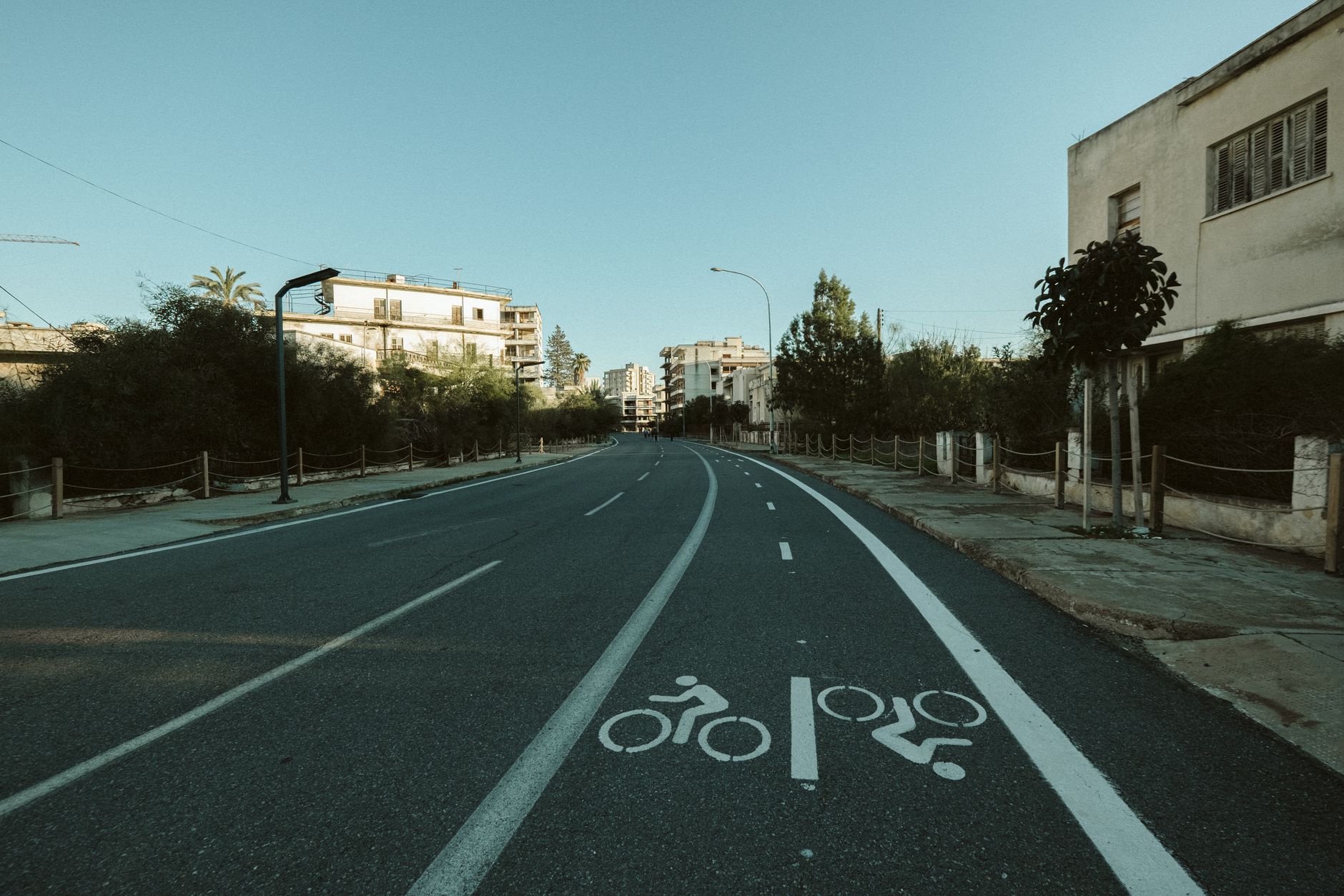 A deserted urban street with a marked bike lane, surrounded by buildings and trees.