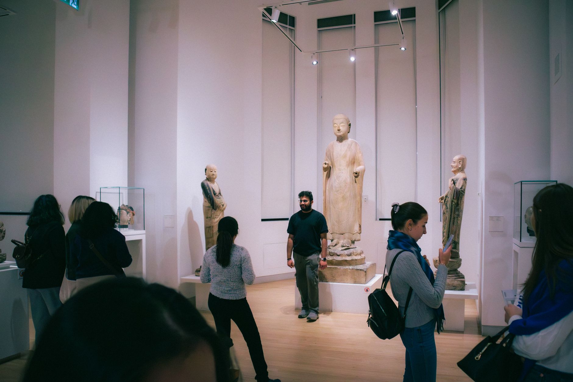 People exploring a Toronto art museum showcasing historic Buddha statues from Chinese culture.