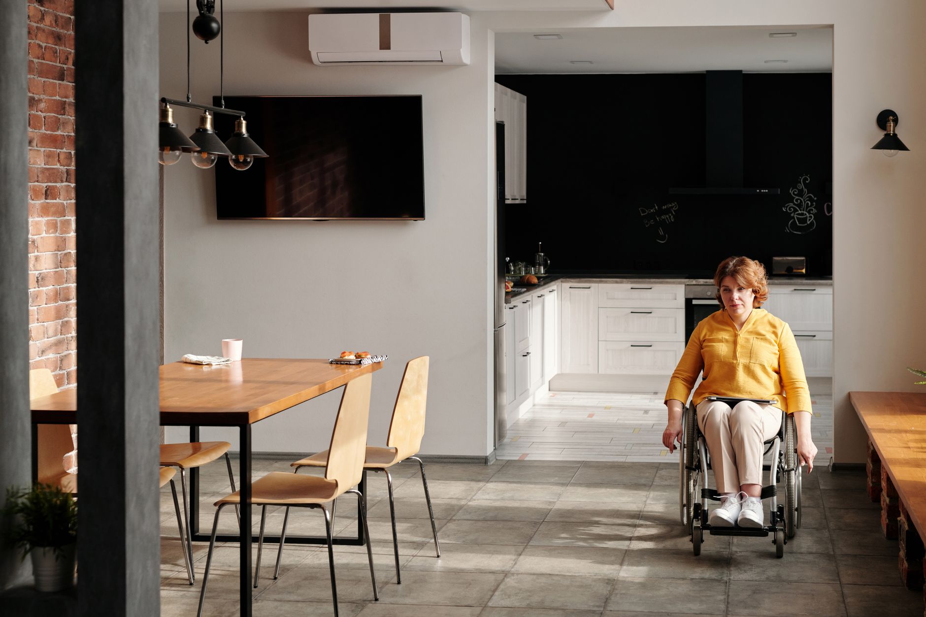 A woman in a wheelchair sits in a modern kitchen, showcasing accessibility in home design.